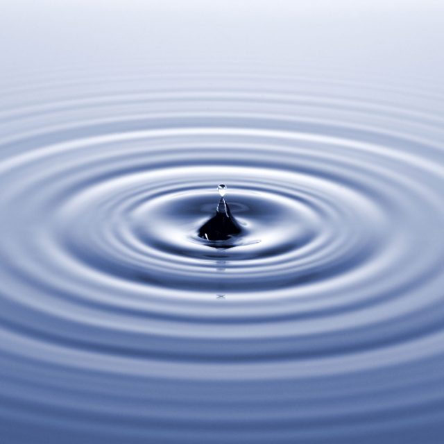 Ein Wassertropfen fällt ins Wasser und erzeugt kleine Wellen.