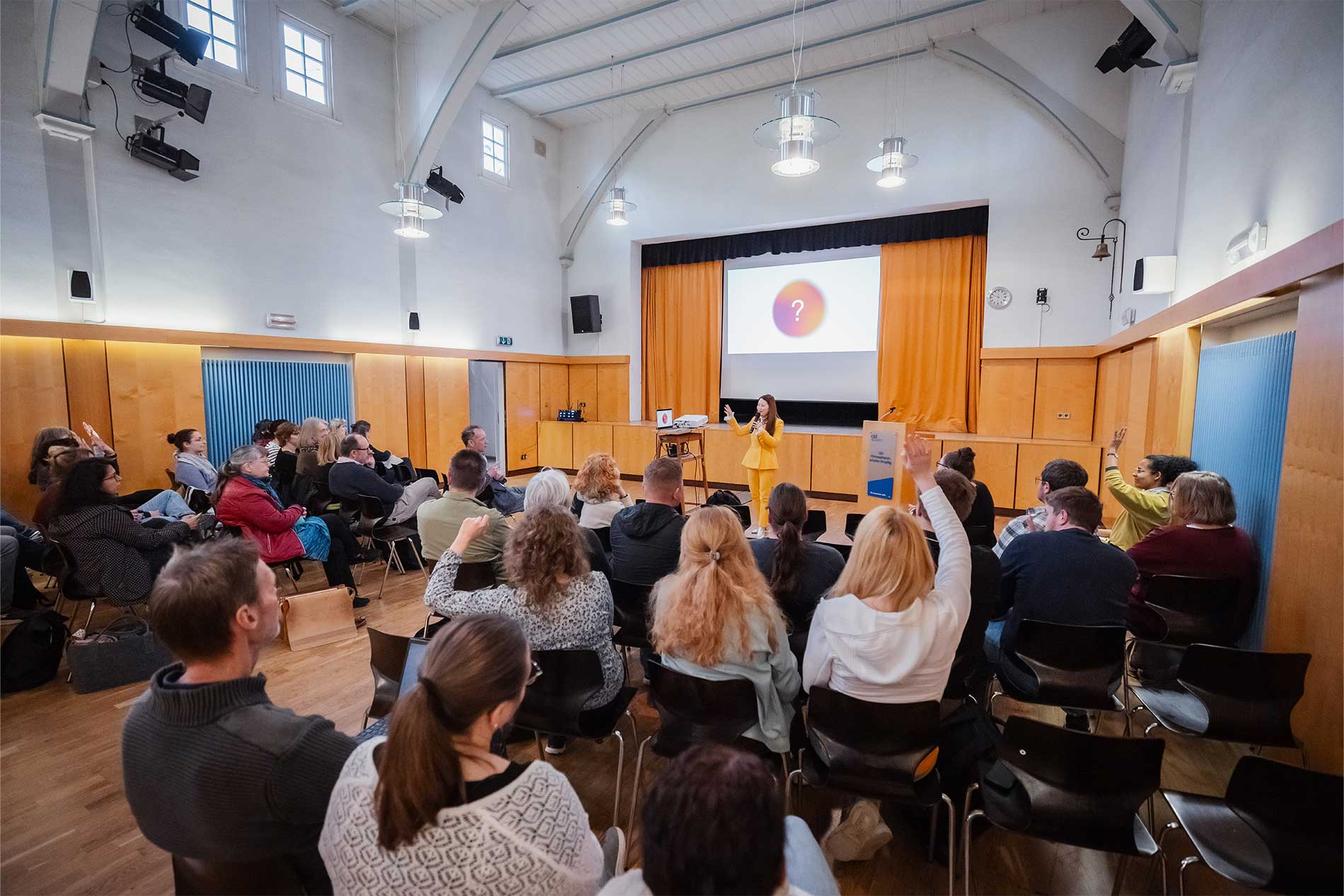 Phuong Tran hält einen KI-Workshop vor dem Kollegium des GSG in Droyßig. Die Teilnehmenden sitzen in einem großen Saal und beteiligen sich aktiv, mehrere Personen melden sich. Im Hintergrund ist eine Präsentationsfolie zu sehen. Das Bild zeigt eine lebendige Workshop-Situation zur praxisnahen Vermittlung von Künstlicher Intelligenz.