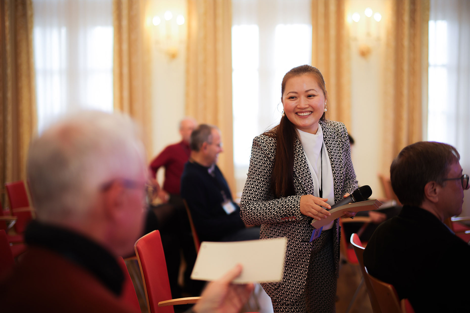 Phuong Tran leitet einen Workshop in Magdeburg und spricht lächelnd mit Teilnehmenden im Raum. Sie hält ein Mikrofon und Moderationskarten in der Hand. Die offene Gesprächssituation zeigt den direkten Austausch und die praxisnahe Vermittlung von Wissen rund um Künstliche Intelligenz.